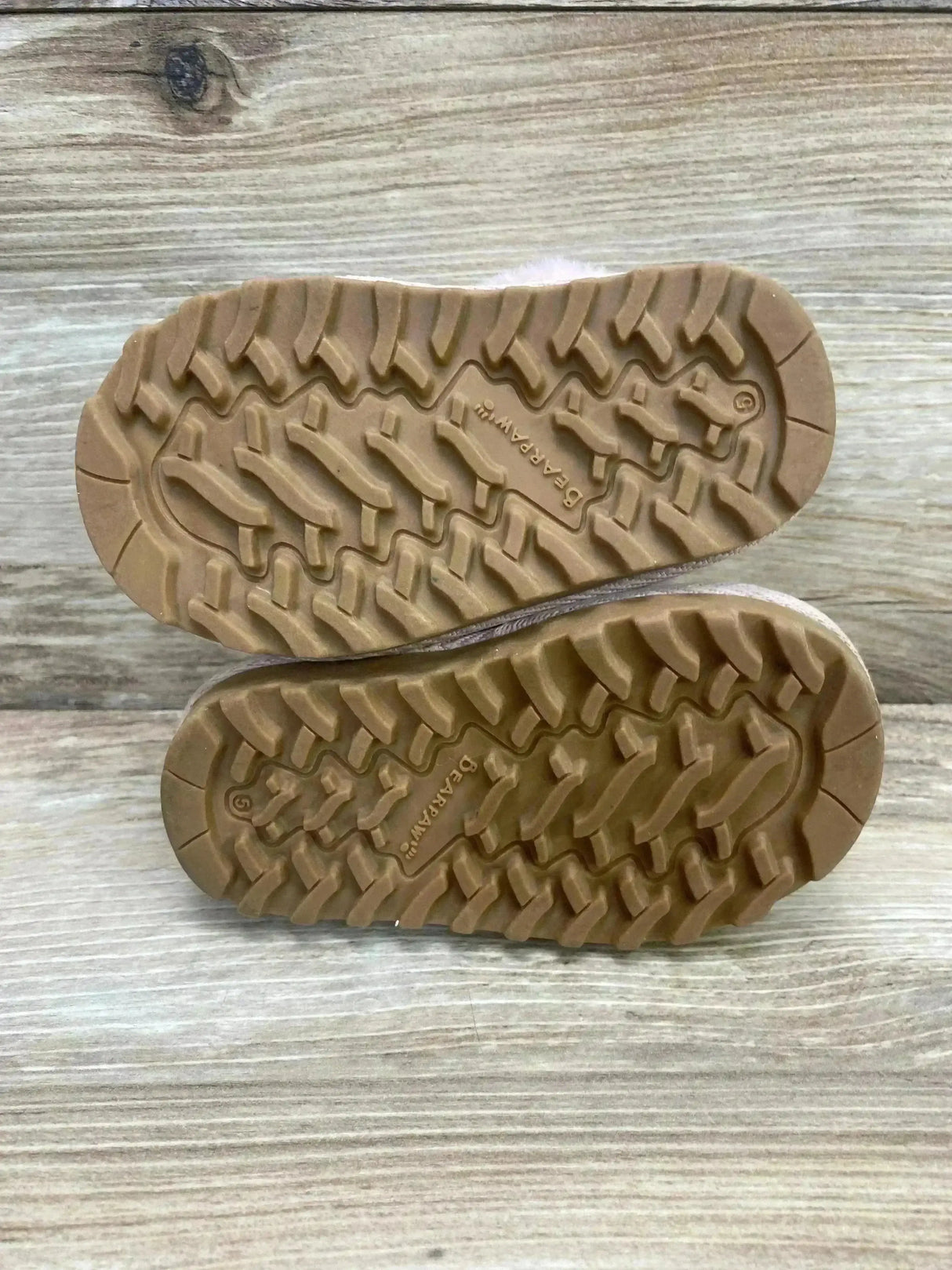 Bottom view of BEARPAW Rebecca suede slippers showcasing rubber tread pattern and stamped BEARPAW logo on wooden surface