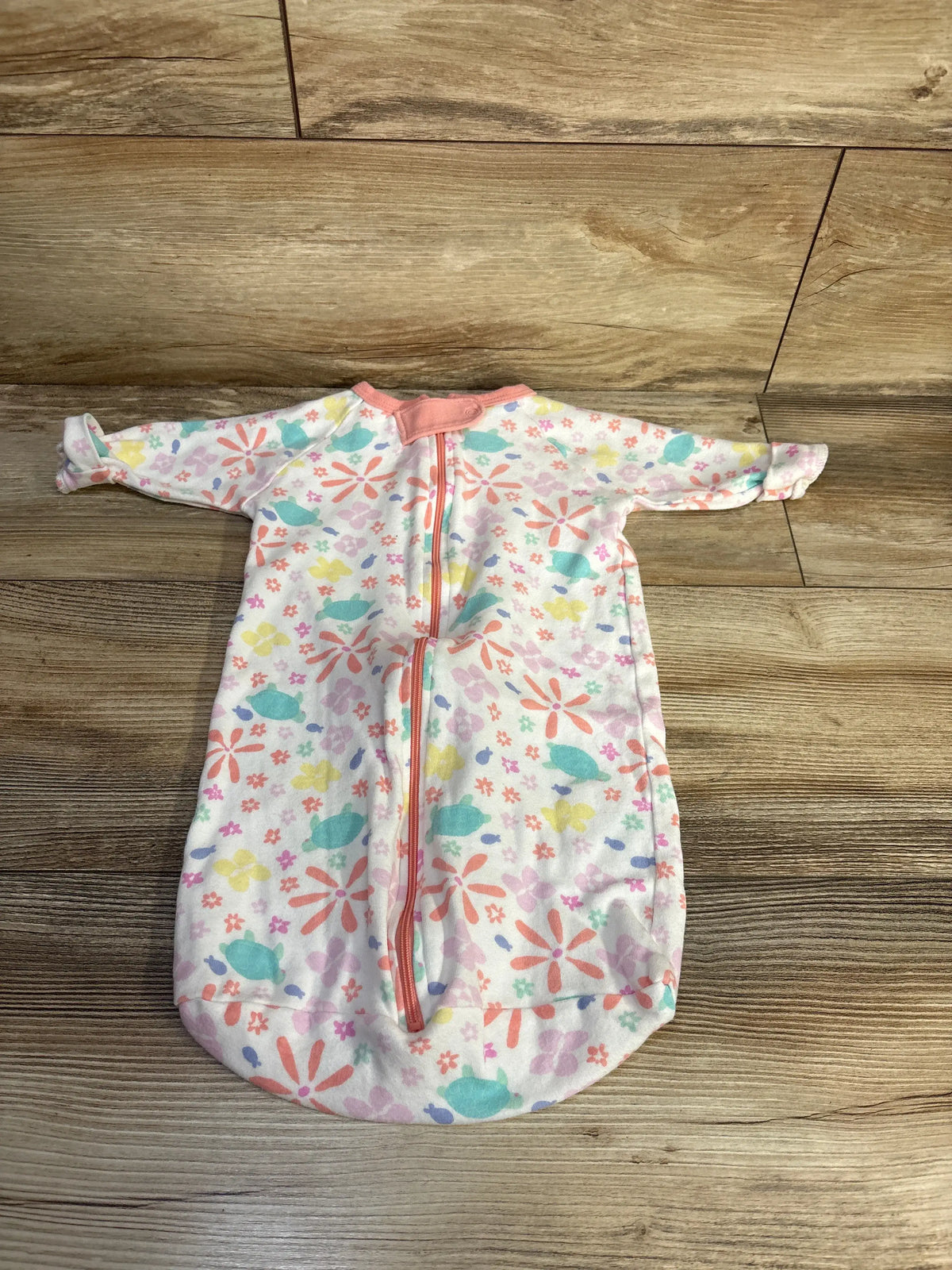 Top view of The Peanutshell sleep sack in size 0-3m, showcasing long sleeves, pink zipper, and floral pattern on a wood-look floor