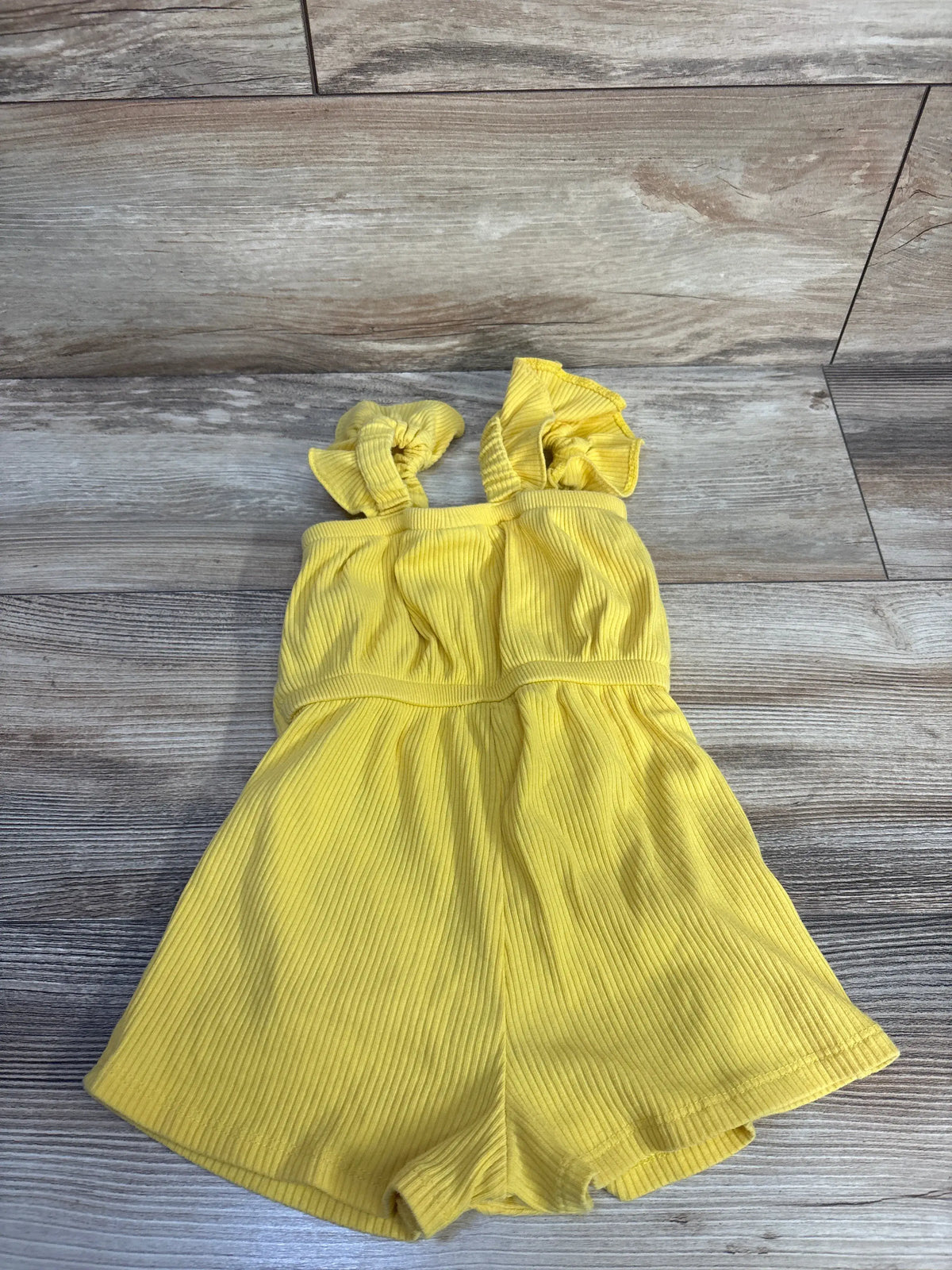 Flat lay of Old Navy yellow ribbed tank shortie romper showcasing tank straps and shortie length on a wood floor