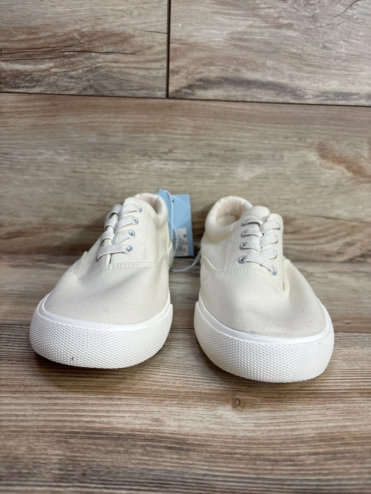 Pair of ivory kids canvas sneakers with white rubber soles on wood floor
