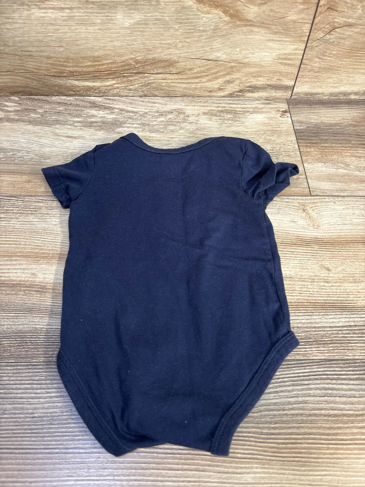 Navy blue short sleeve baby bodysuit laid flat on a wooden surface.