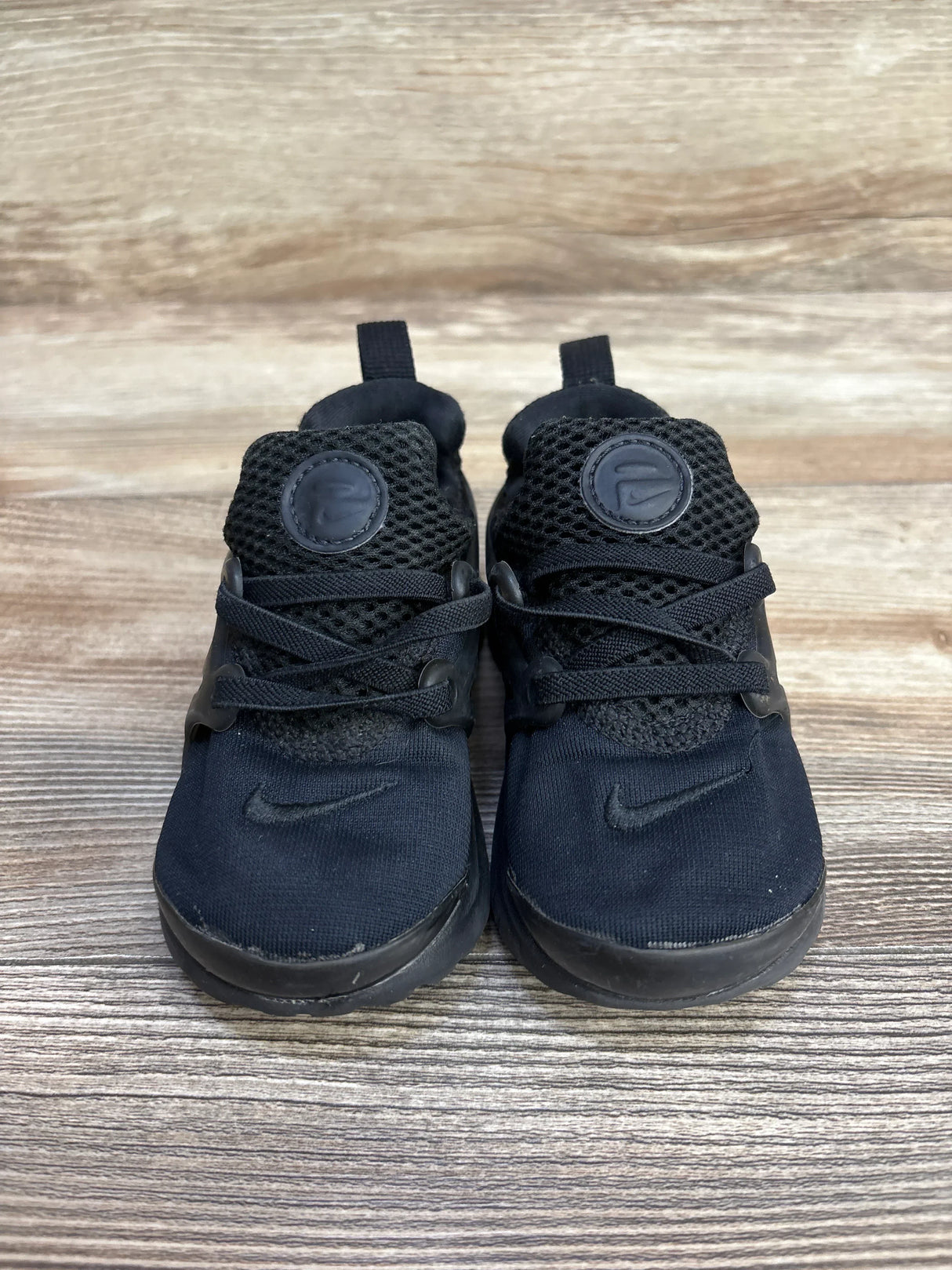 Black Nike toddler sneakers with mesh uppers on wooden floor