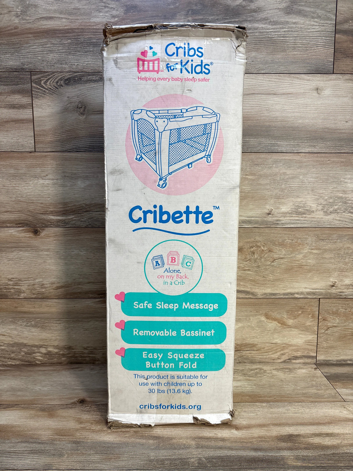 Cribette portable crib box on wood floor, Cribs for Kids branding, safe sleep features listed