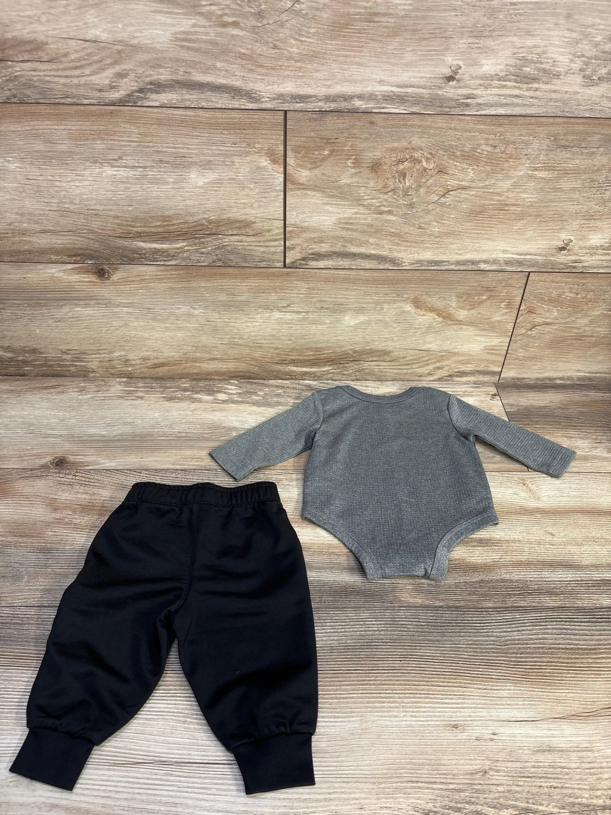 Top-down view of Nike grey ribbed bodysuit and black joggers, 3M, showing elastic waistband and cuffed ankles on wood