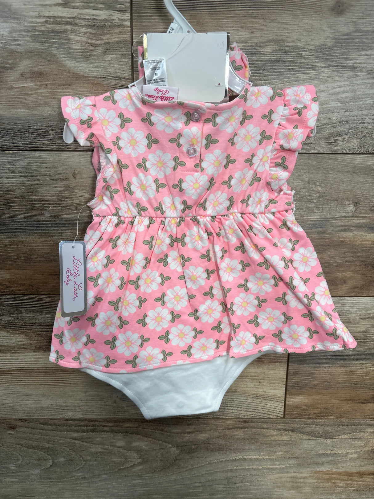 Pink floral baby romper dress with ruffle sleeves, white floral print, on wood background