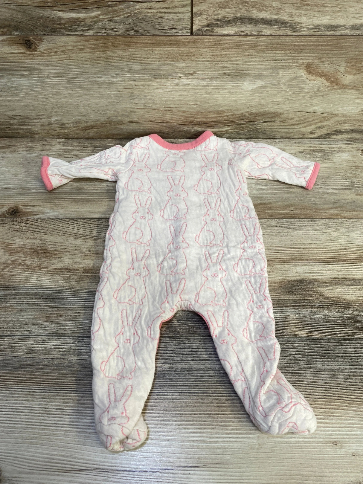 Flat lay of Baby Gap pink footed sleeper 0-3 months showing all-over stitched bunny outlines, long sleeves, and pink trim on wood background