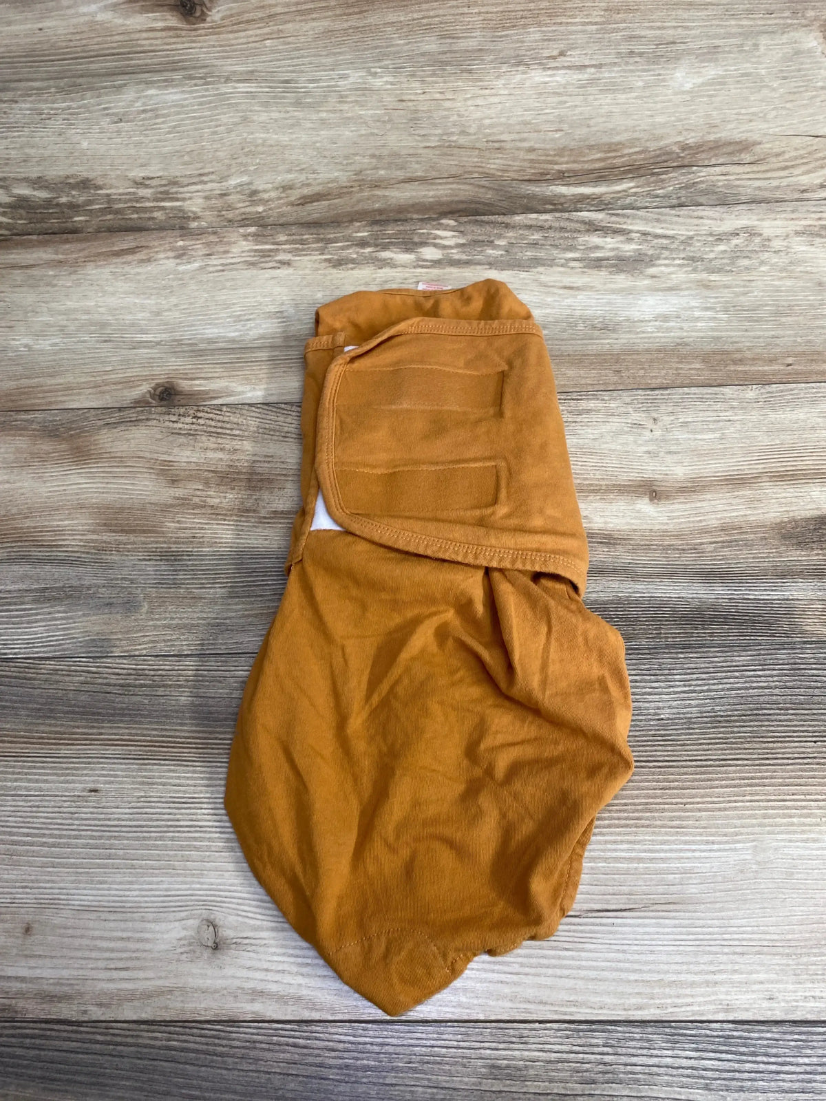 Flat-lay of Embe Starer newborn swaddle in sand, size 0-3m, showing folded swaddle with Velcro fastener on wooden floor