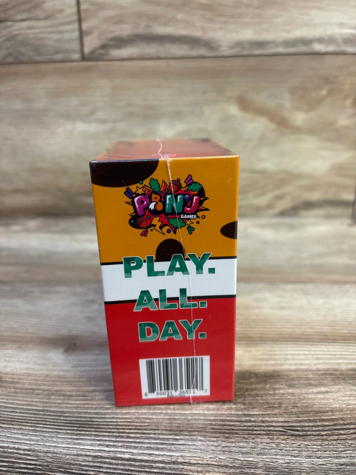Front view of Chicken or Cheetah card game box showing large PLAY. ALL. DAY. text and colorful logo on wood tabletop