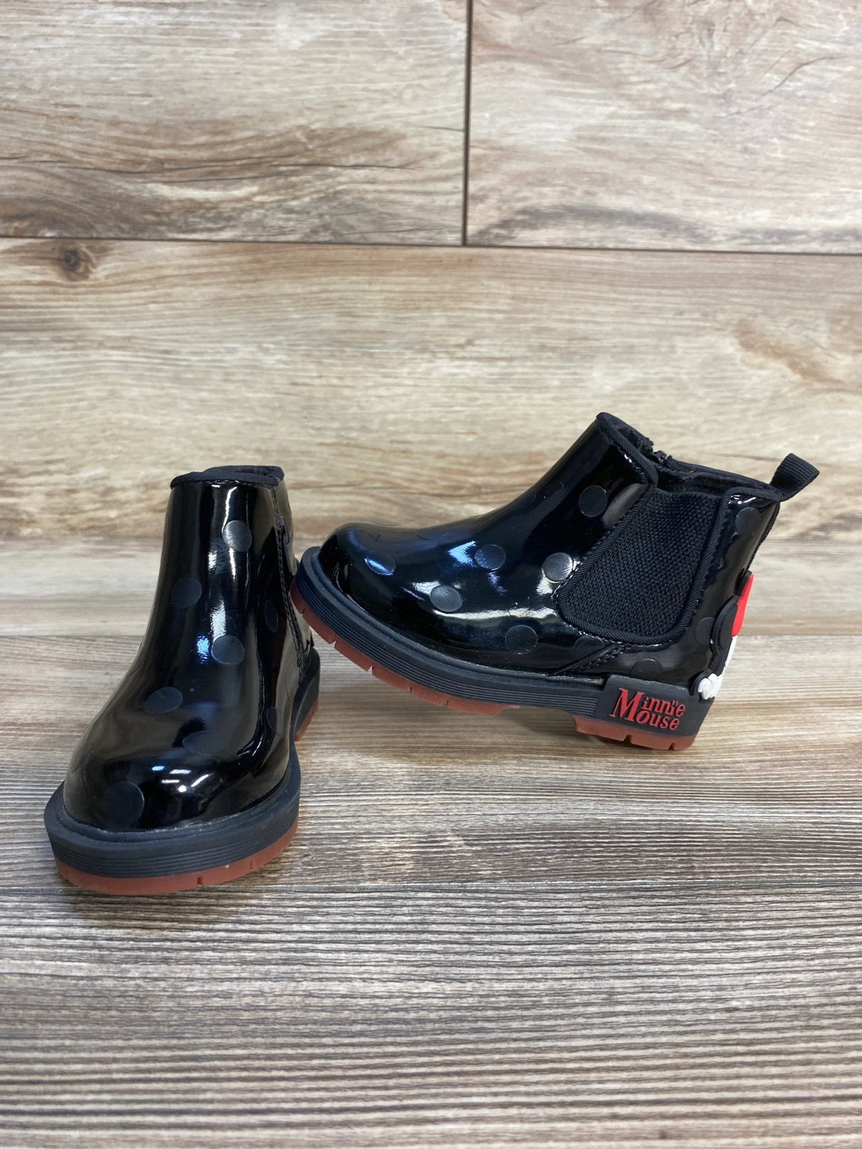 Black Minnie Mouse kids rain boots with polka dots and red soles on wood floor