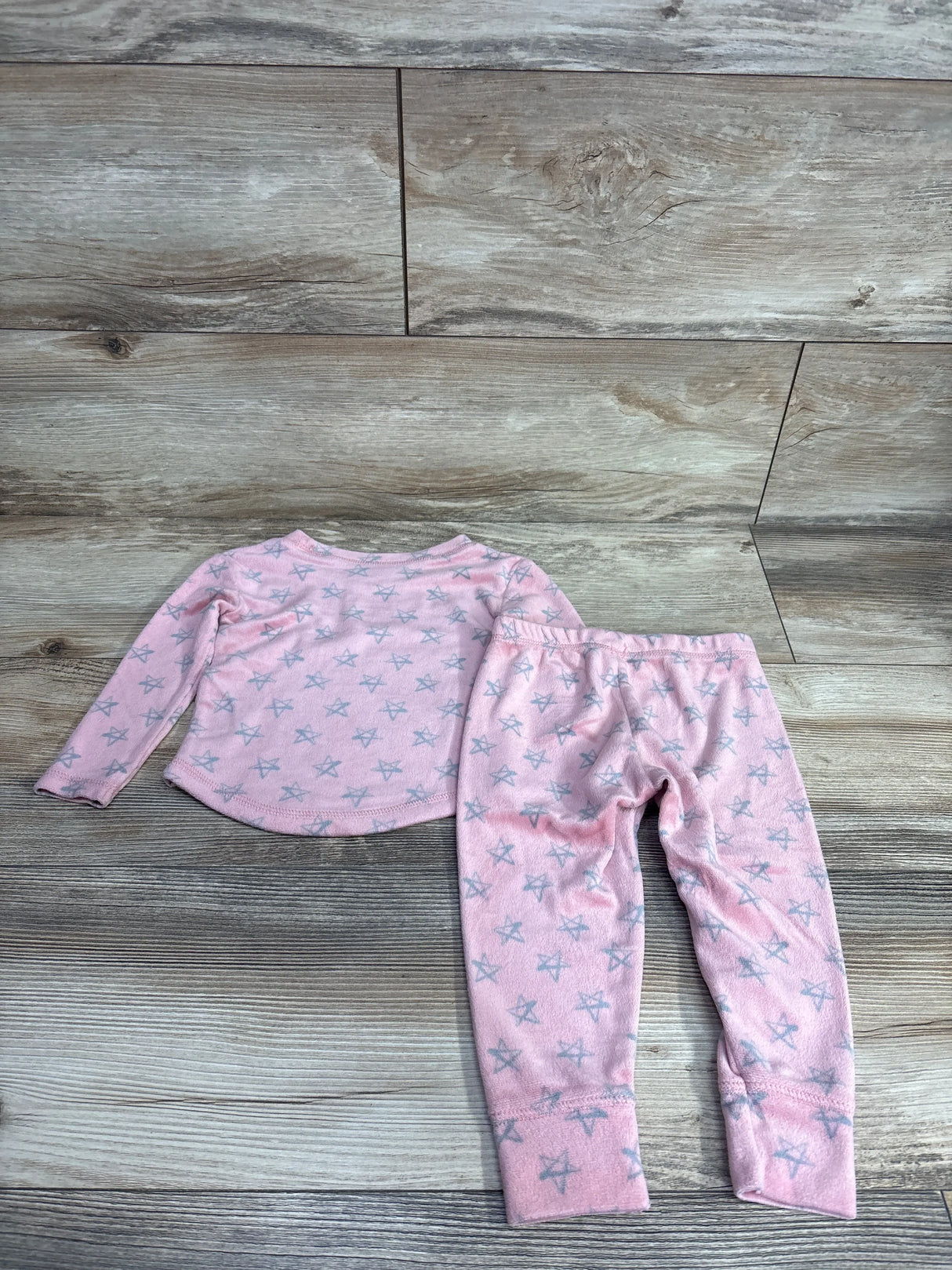 Pink toddler pajama set with gray star patterns, long-sleeve top and pants on wooden floor
