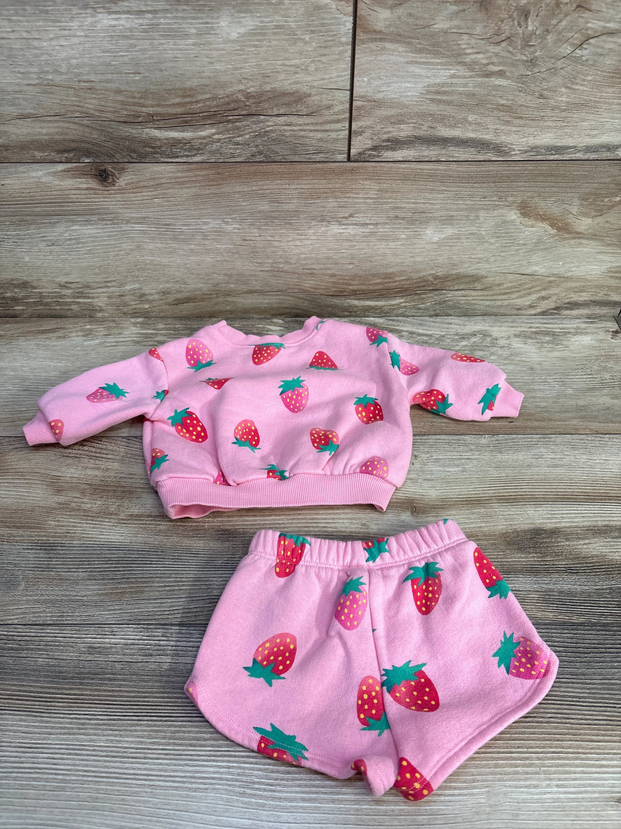 Pink baby pajama set with strawberry print, long-sleeve top and shorts on wooden floor