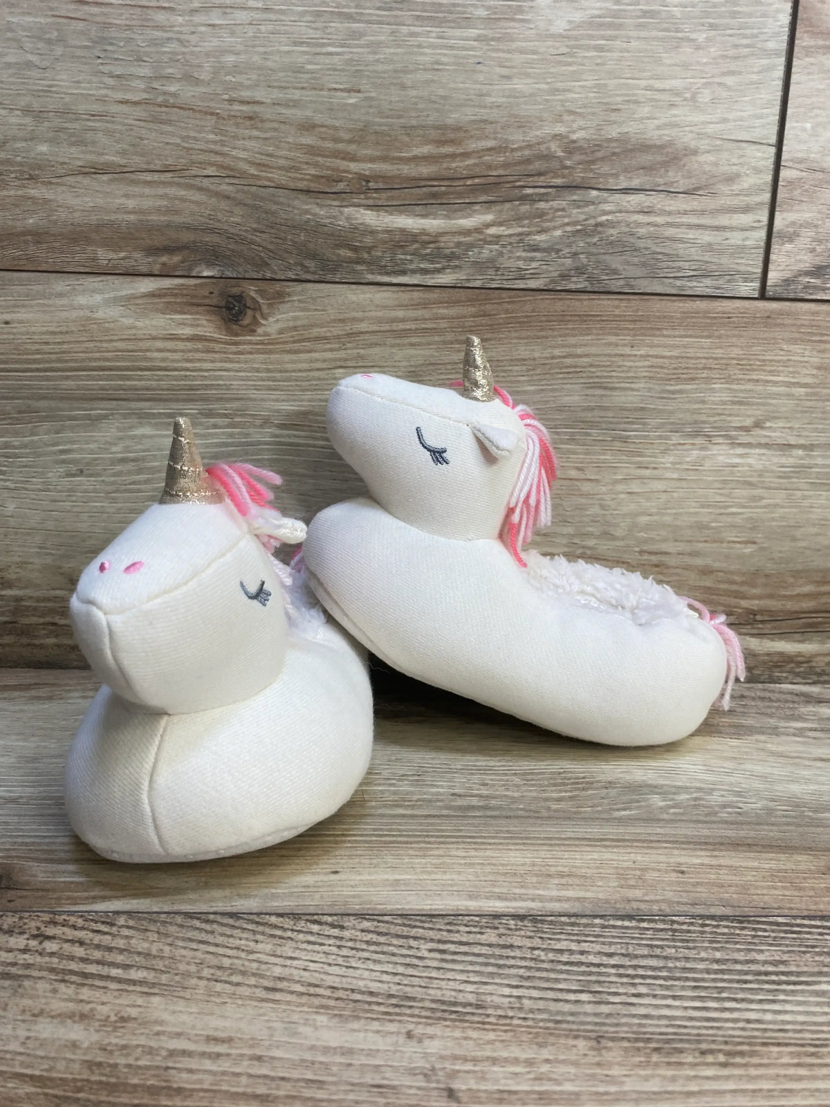 Plush unicorn baby slippers with gold horns and pink manes on wood background