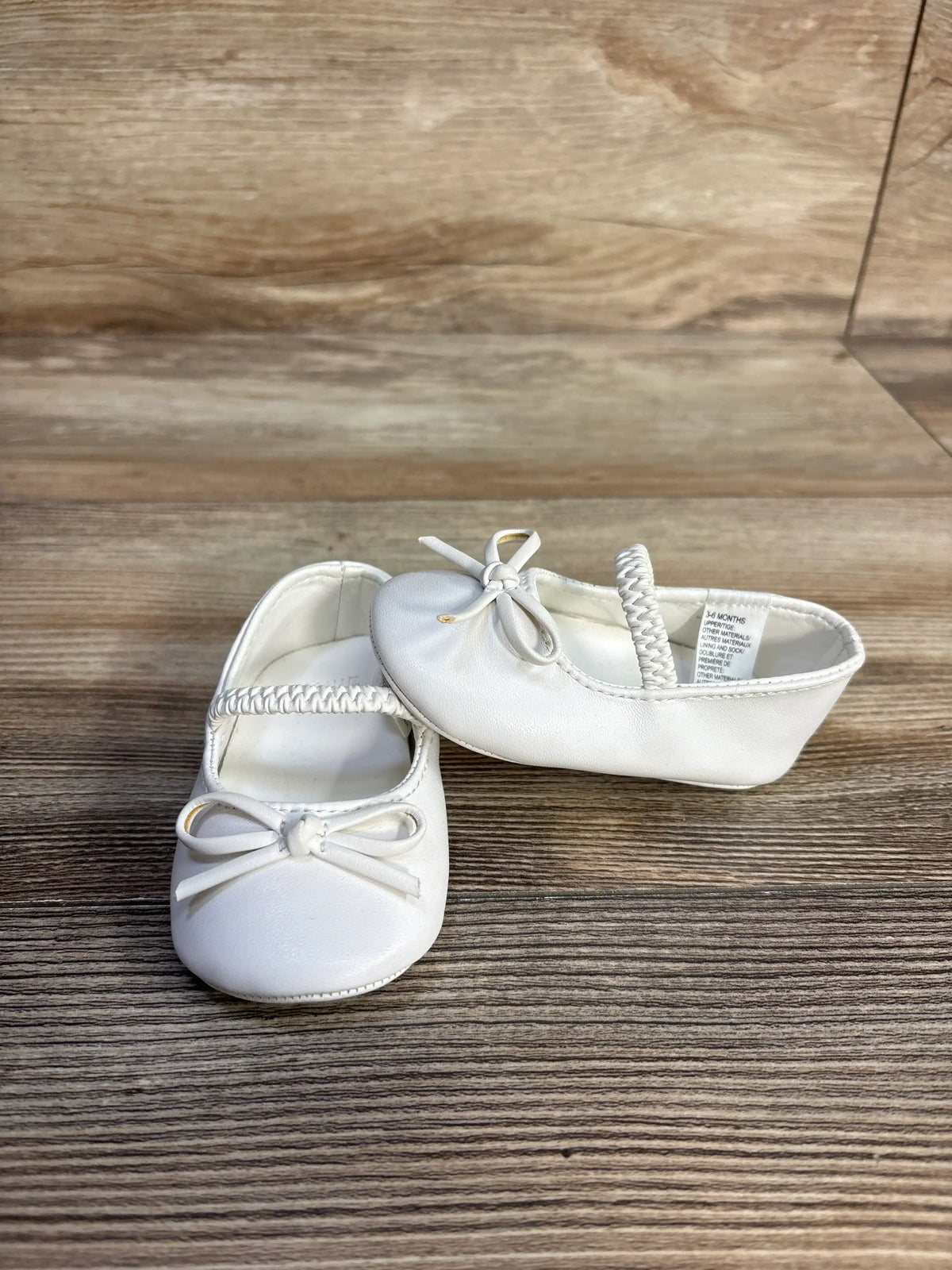Pair of white Me n Mommy To Be bow soft sole ballet flats for toddlers on a wooden surface