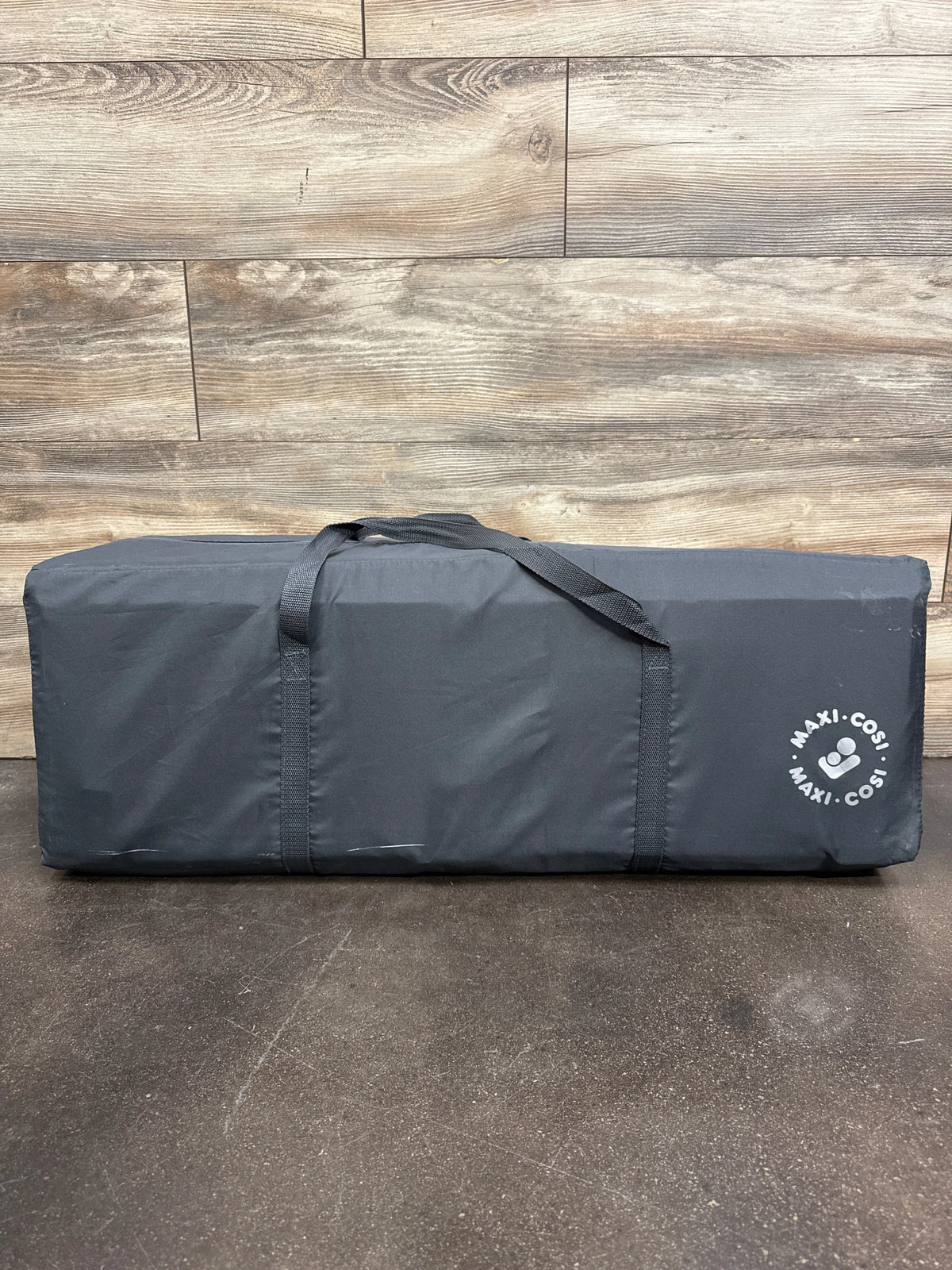 Front view of Maxi-Cosi Swift Playard in Grey travel bag with carrying straps on a wood floor