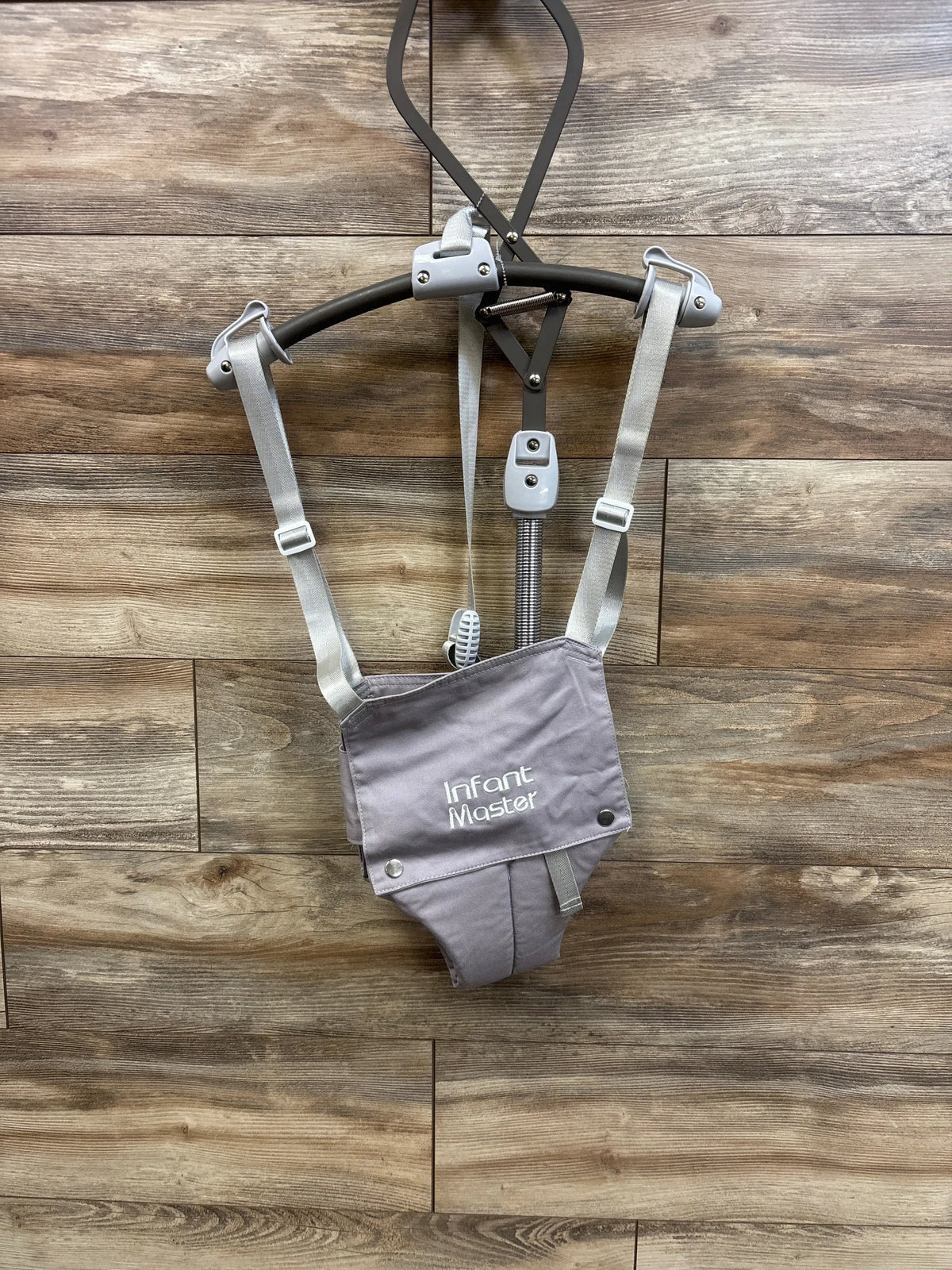 Grey Infant Master doorway jumper baby gear hanging against a wooden wall background