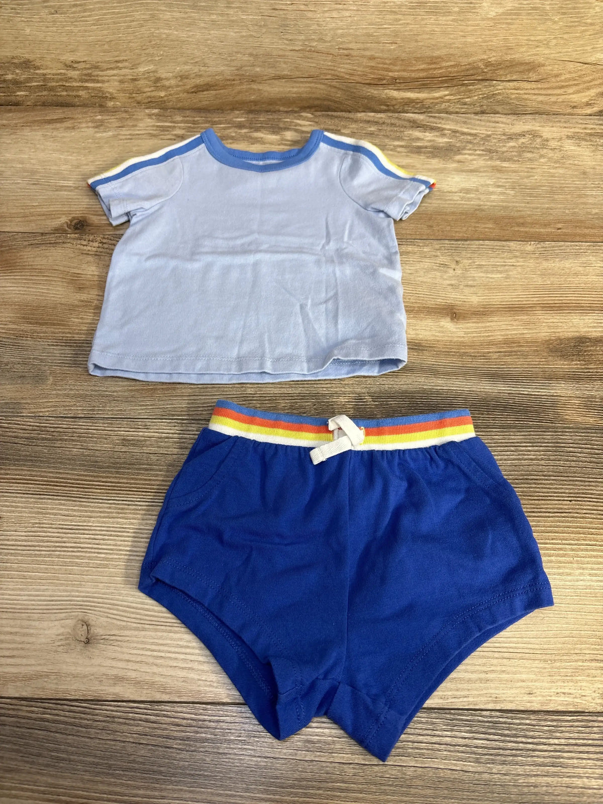 Flat lay of Cat and Jack baby 2-piece light blue tee and blue shorts with rainbow elastic waistband on wood background