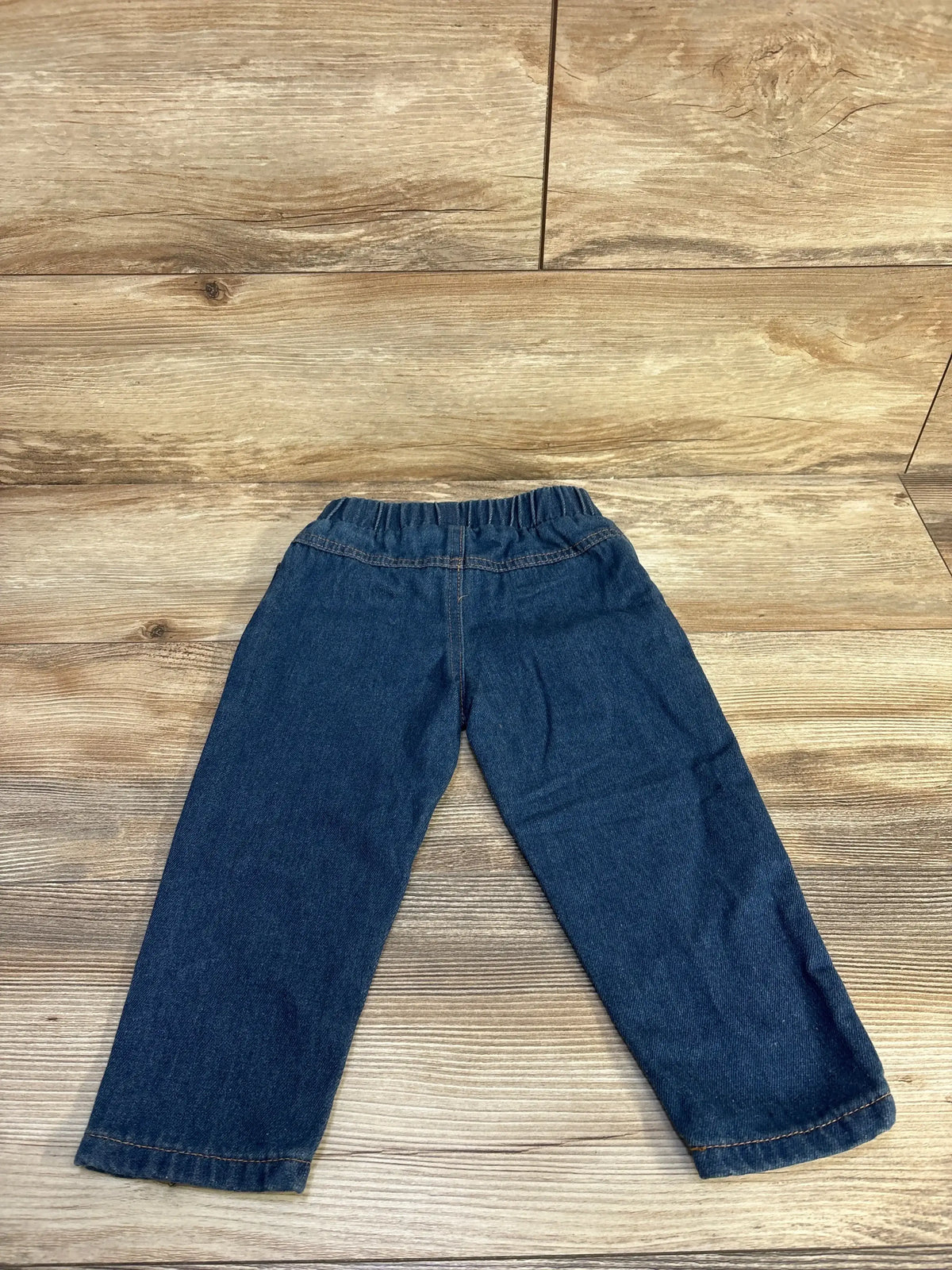 Flat lay of toddler blue distressed pull-on jeans showcasing elastic waistband and straight legs on wood background