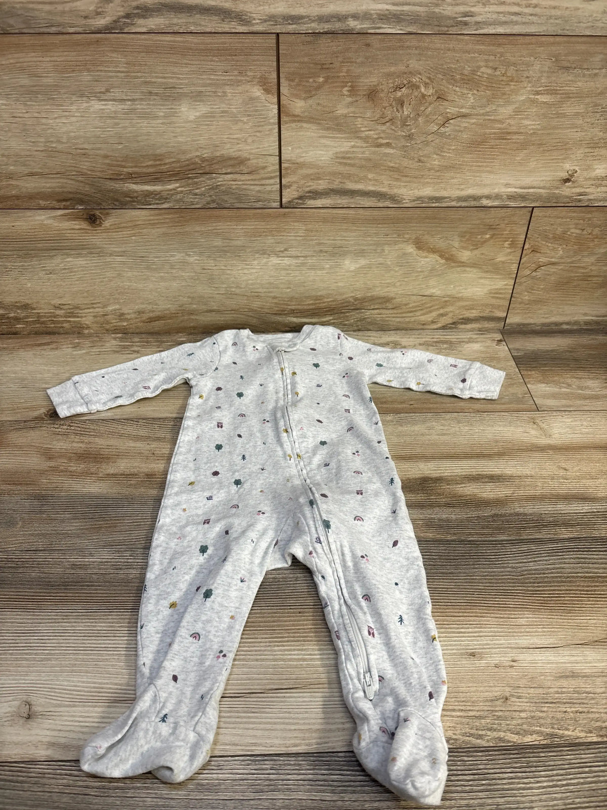 Flat lay of grey Little Planet organic footed sleeper showcasing front zipper and small multicolor tree and rainbow prints on wood floor