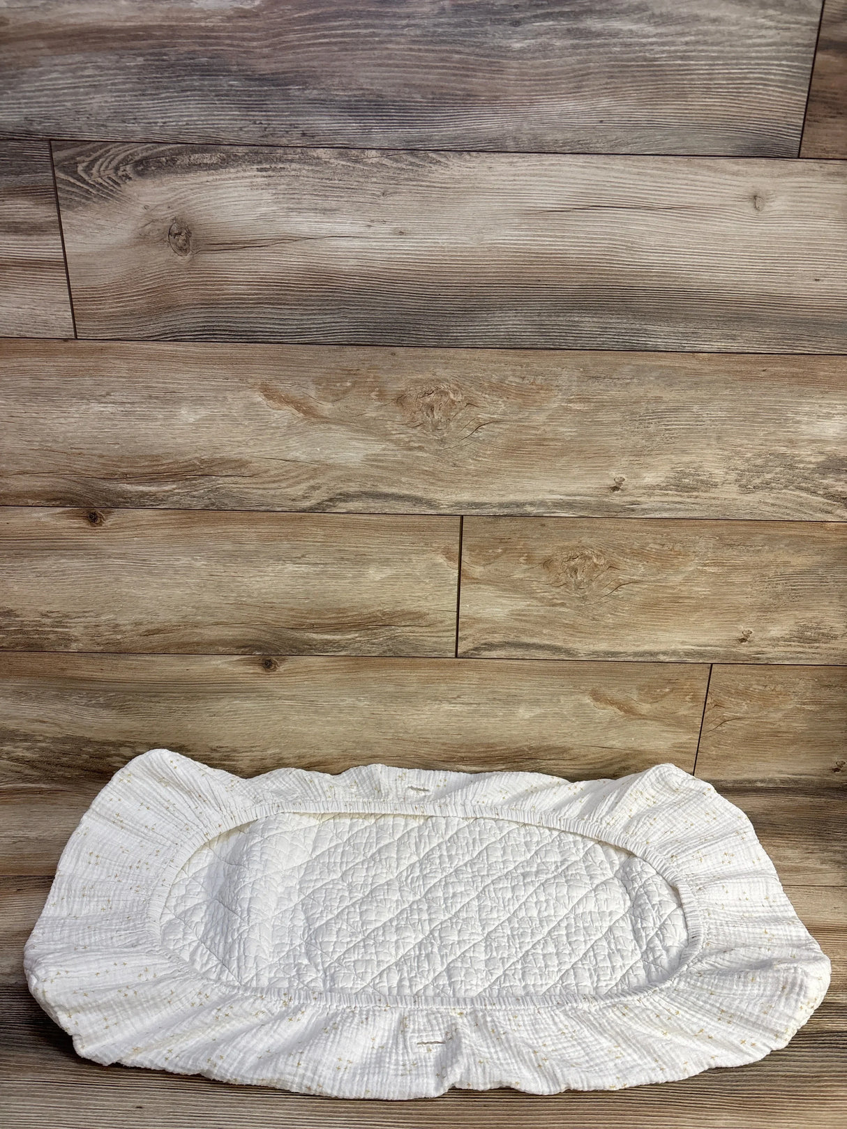 Top view of Crate Kids gauze changing pad cover with gold stars, ruffled trim and quilted center on wood background