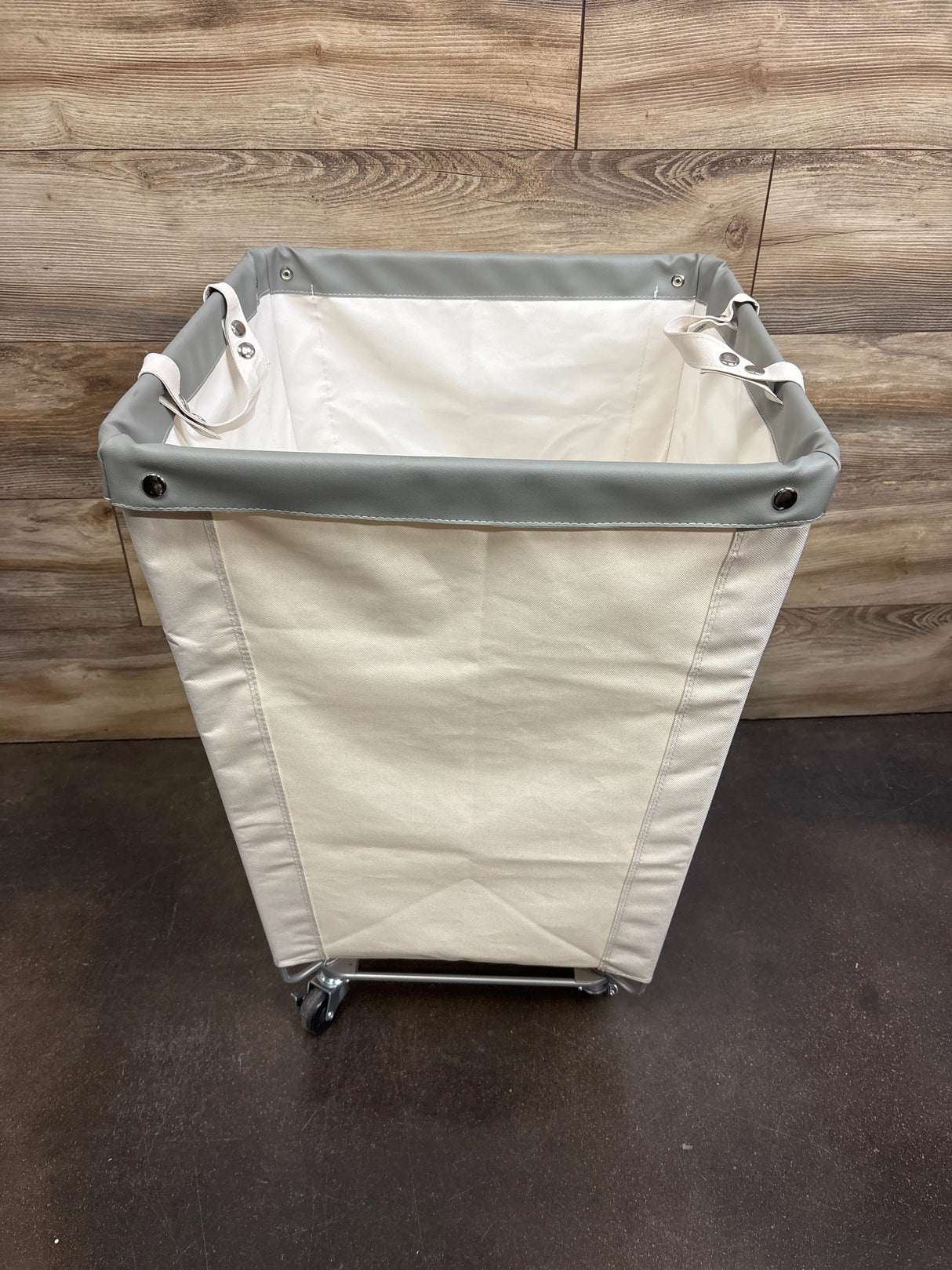 Top-front view of Seville Classics natural white rolling canvas laundry hamper showcasing gray vinyl rim, interior canvas lining, and caster wheels on wood-panel background