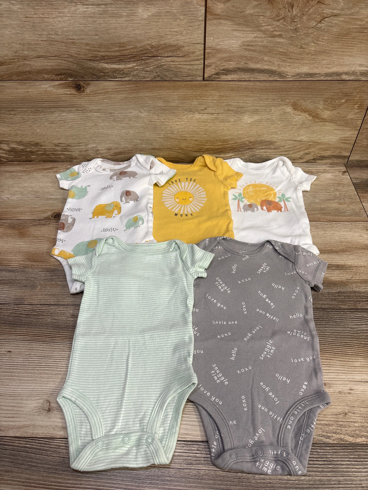Top view of Carter’s 5 pack bodysuits in varied colors and patterns, size 3 months, on a wood surface