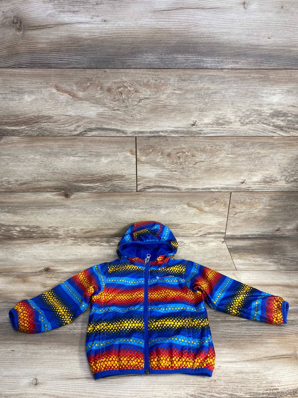 Front flat lay of Columbia Mini Pixel Grabber III wind jacket 18-24M showing hood, full zipper and multicolor dot-stripe print on wood floor