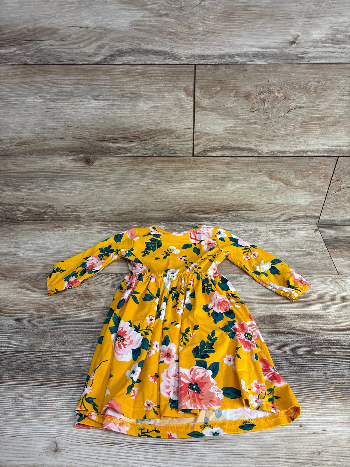 Yellow long-sleeve toddler dress with pink and white floral print on wooden floor