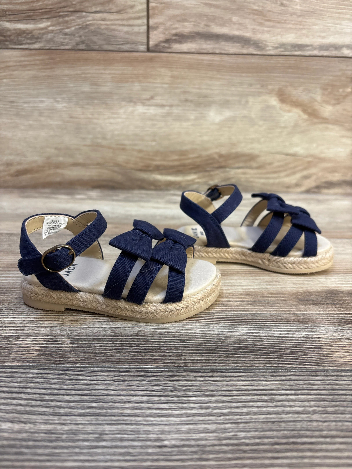 Navy blue toddler sandals with bows and woven soles on wood background