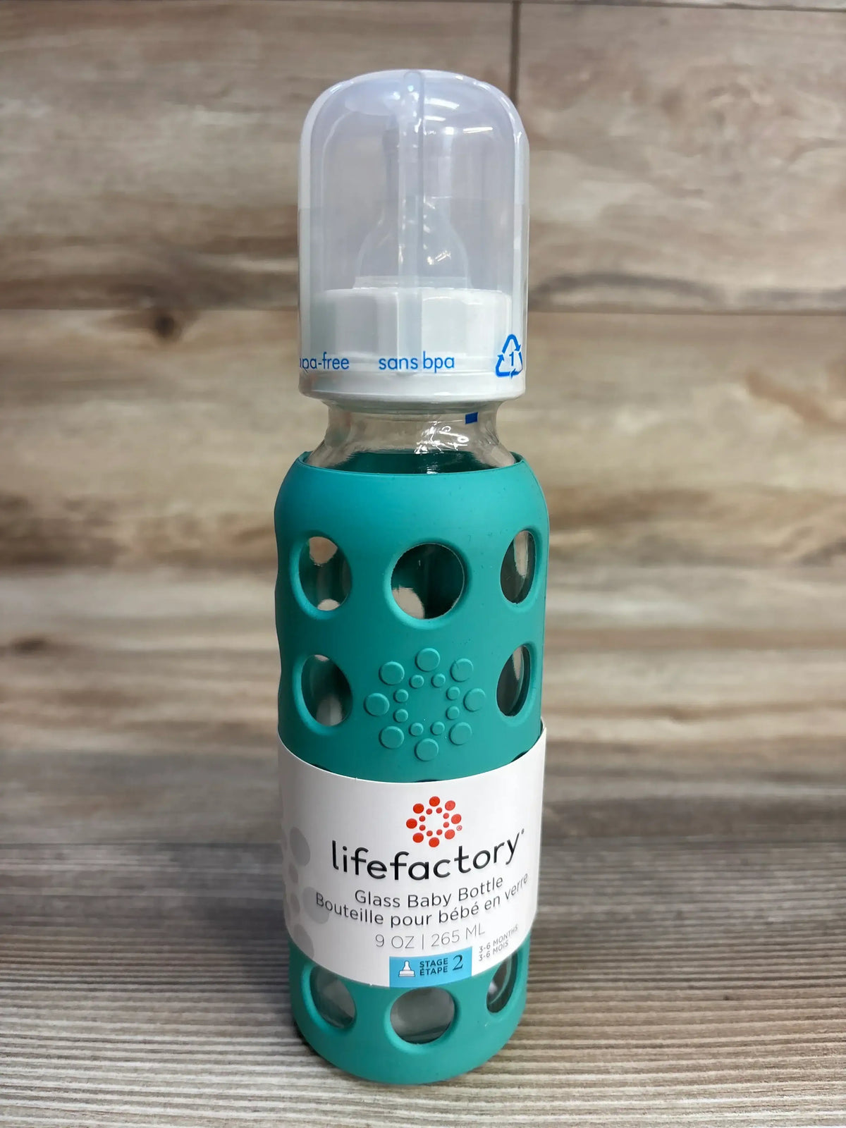Lifefactory glass baby bottle with teal silicone sleeve and BPA-free cap on wood surface