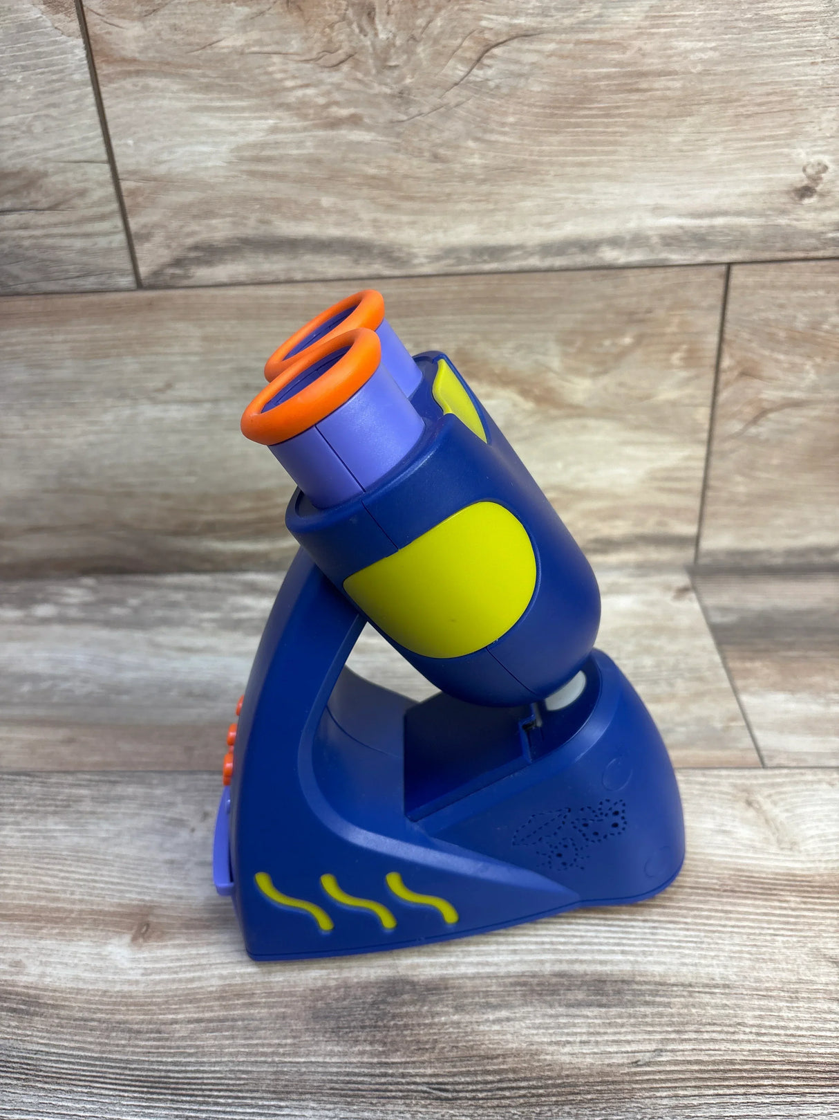Side view of GeoSafari Jr. Talking Kids Microscope showcasing dual purple eyepieces with orange rims and yellow accent panels on wood background