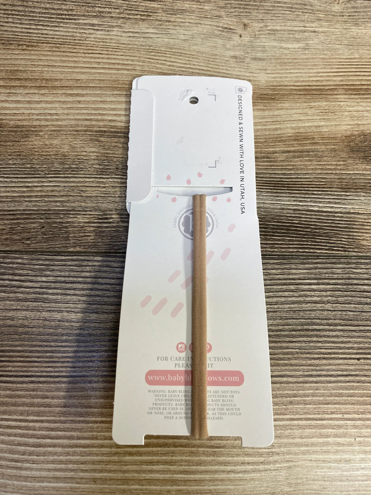 Flat lay of Baby Bow Headband packaging showing nude nylon headband on branded card on wood surface