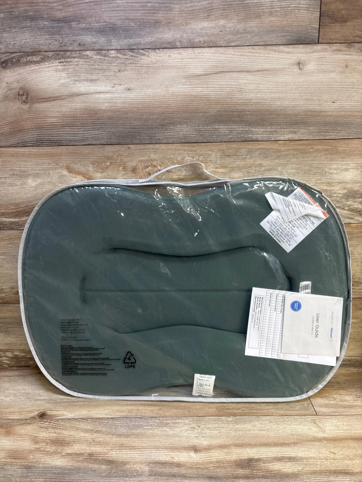 Top-down view of Snuggle Me Curve Lite lounger with moss green cotton cover and contoured foam in clear bag on wood floor