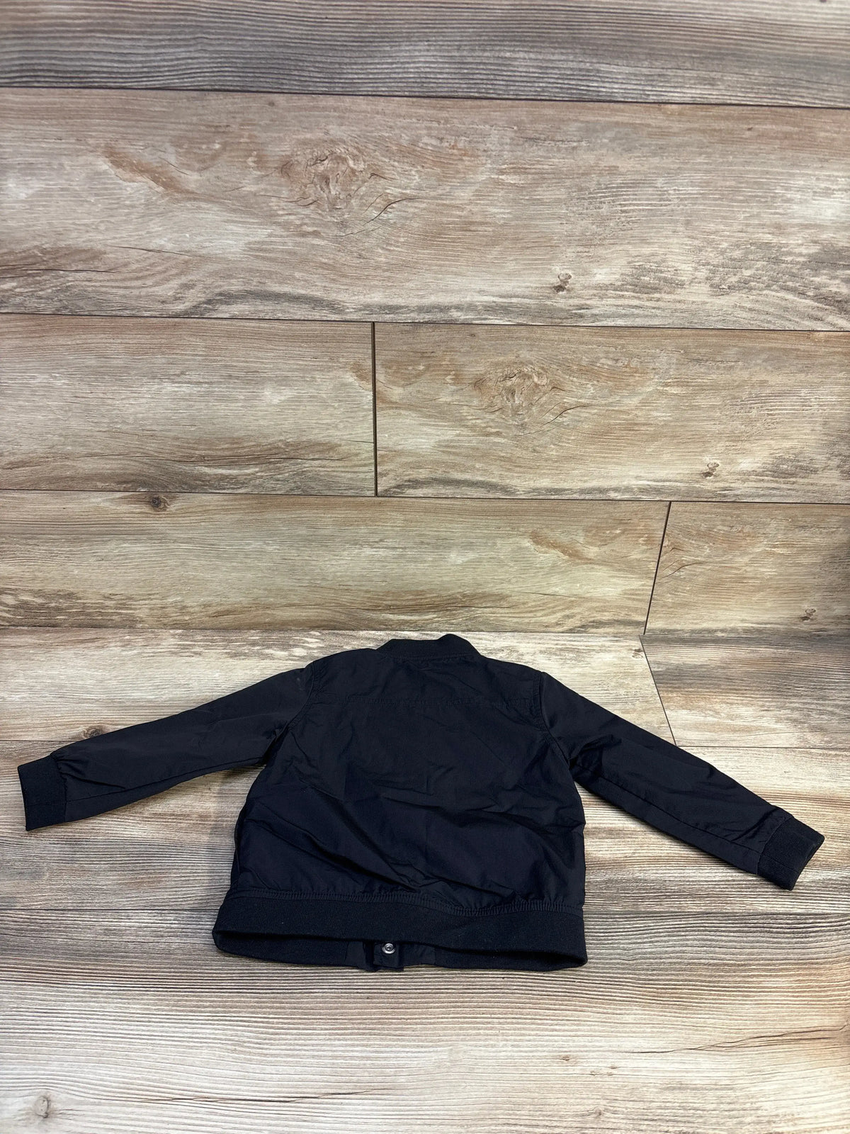 Back view of toddler utility jacket (size 2T) showcasing ribbed cuffs and hem and long sleeves on light wood plank background