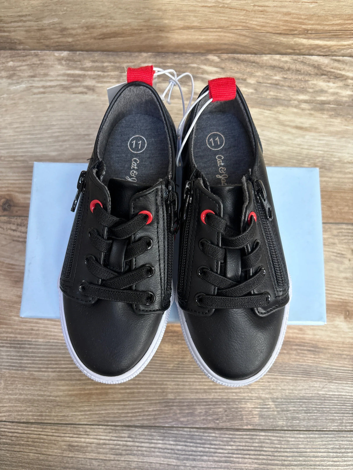 Black youth sneakers with red pull tabs and side zippers on wood floor