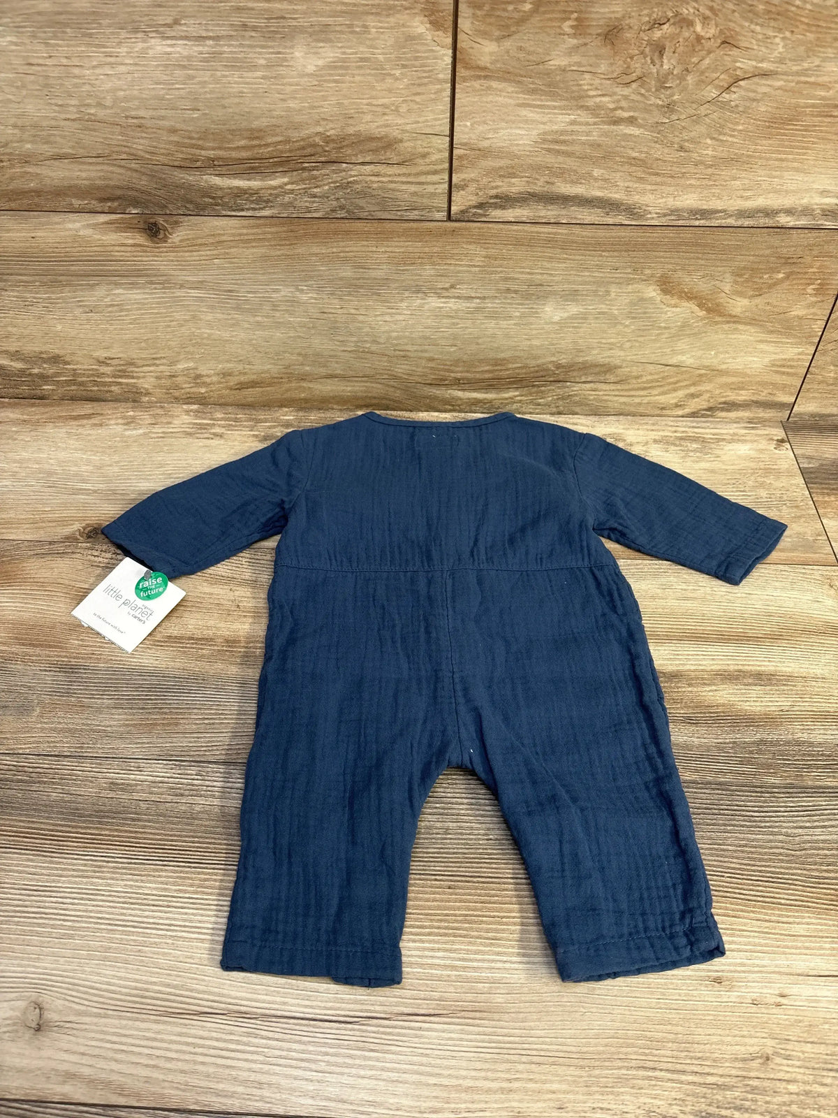 Flat-lay back view of Little Planet muslin jumpsuit in navy blue, size 3 months, showing long sleeves and full-length legs on wood background