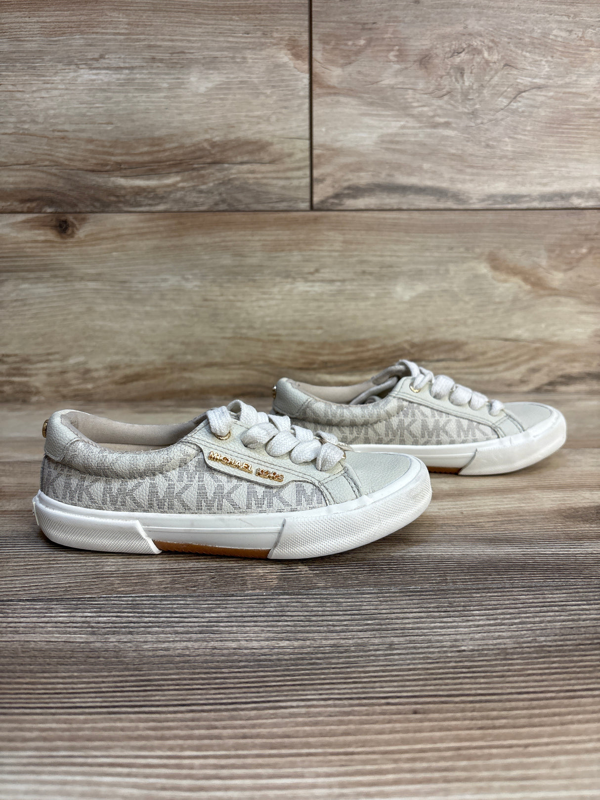 Michael Kors kids sneakers with logo print, white laces, and gold branding on wood floor