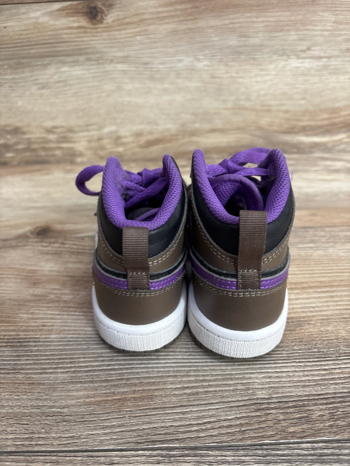 Back view of children's brown sneakers with purple lining and white soles on wood floor