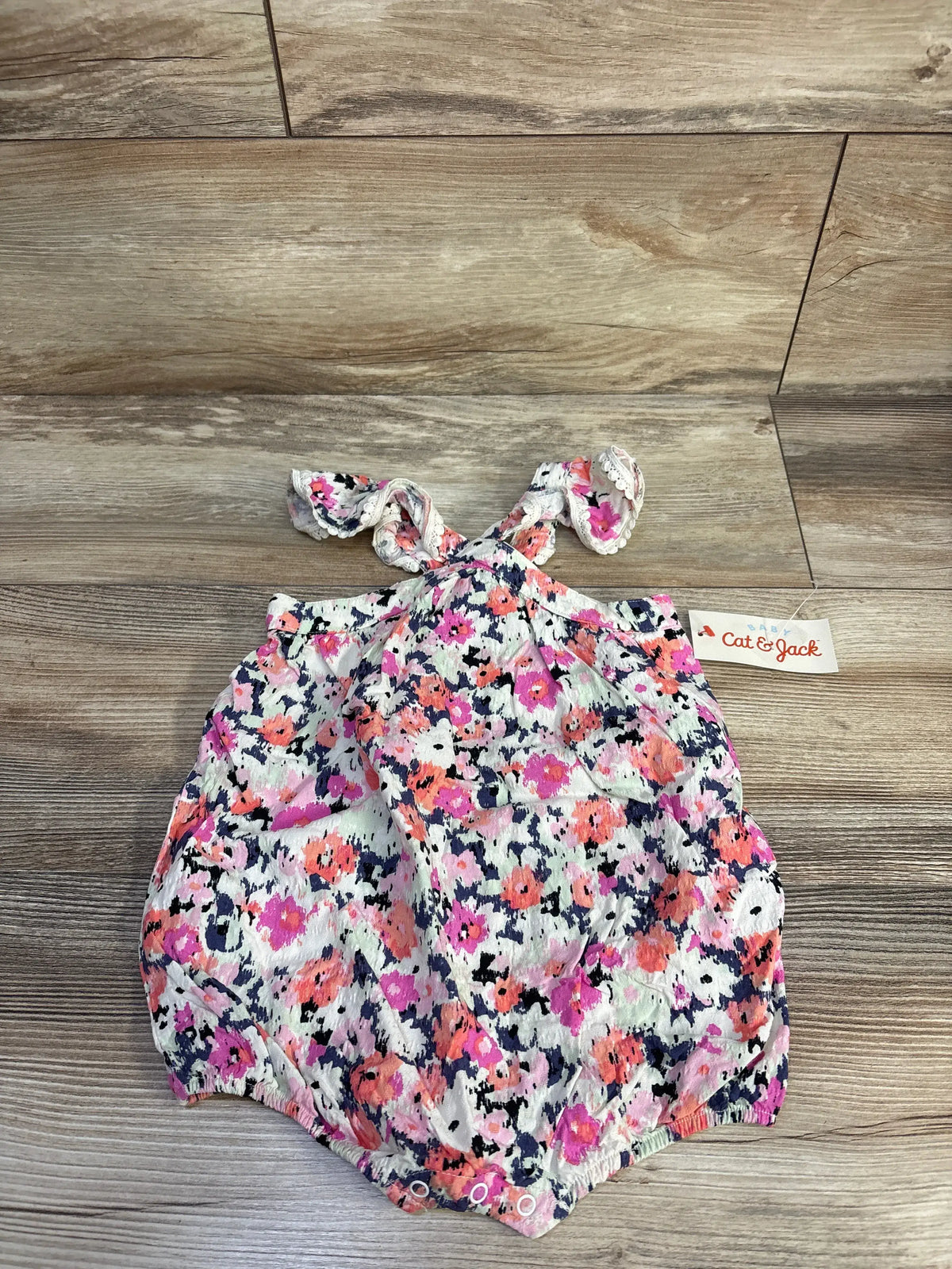 Top view of Cat & Jack pink floral flutter sleeve romper for 6-9 months showcasing one-piece design on a wood floor