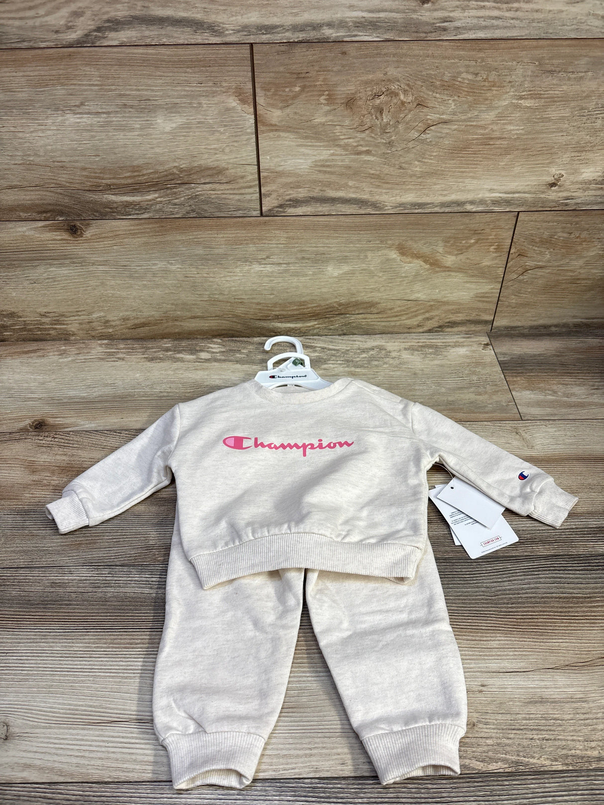 Flat lay of Champion sweatshirt and joggers in beige showing pink logo and ribbed cuffs on wood background