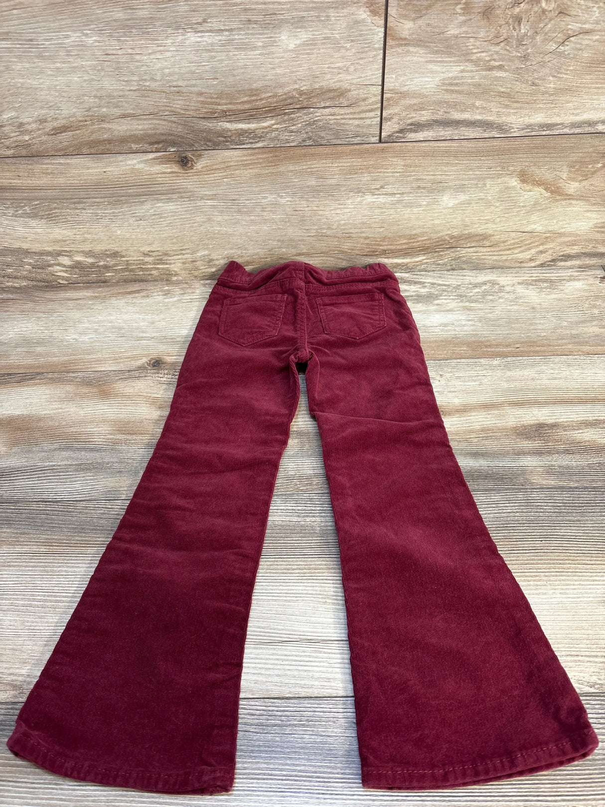 Burgundy kids corduroy bell-bottom pants with back pockets on wood floor