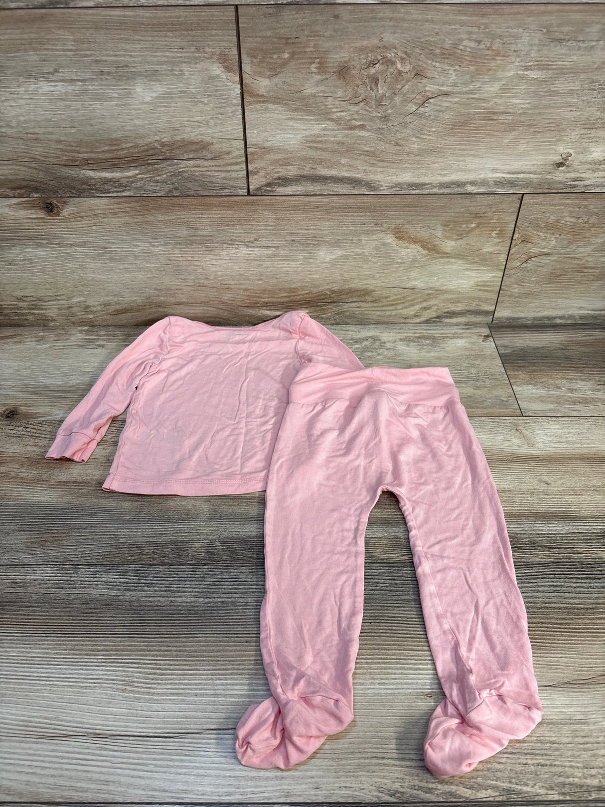 Pink baby pajama set with long sleeves and footed pants on wood floor
