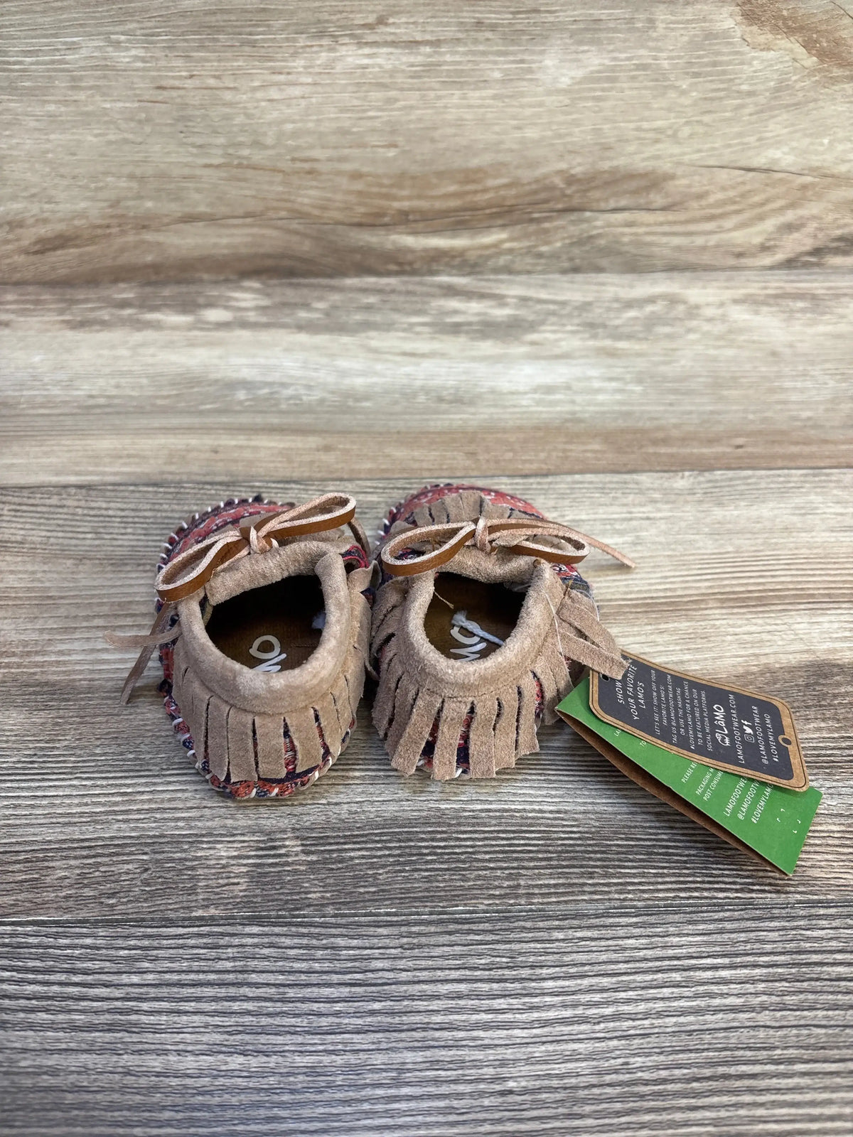 Tan suede baby moccasins with fringe and bows on wood background, resale kids shoes