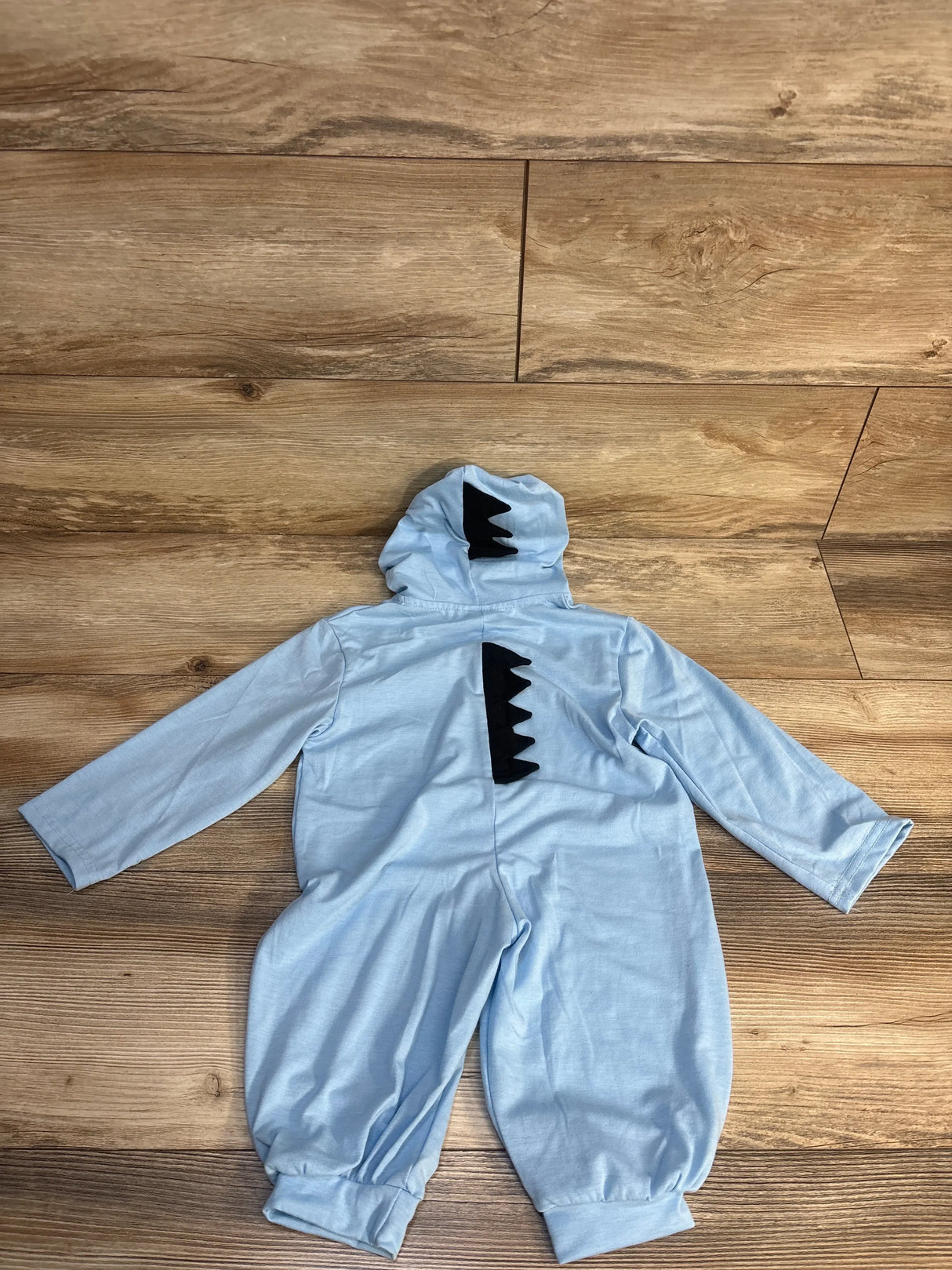 Light blue baby romper with dinosaur spikes on hood and back, laid on wood floor