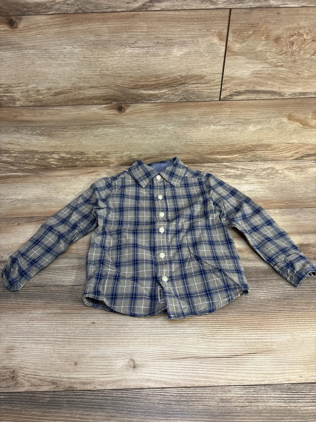 Flat lay of OshKosh toddler plaid button-up shirt size 4T showing front buttons and collar on wood floor background