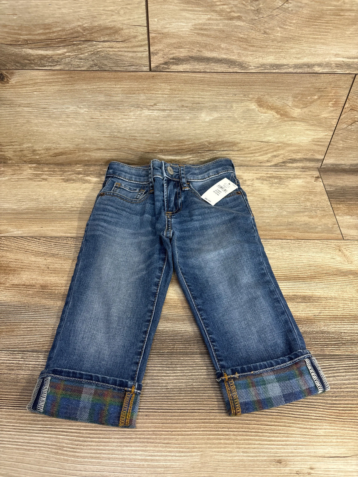Kids blue denim jeans with plaid cuffed hems displayed on wood floor
