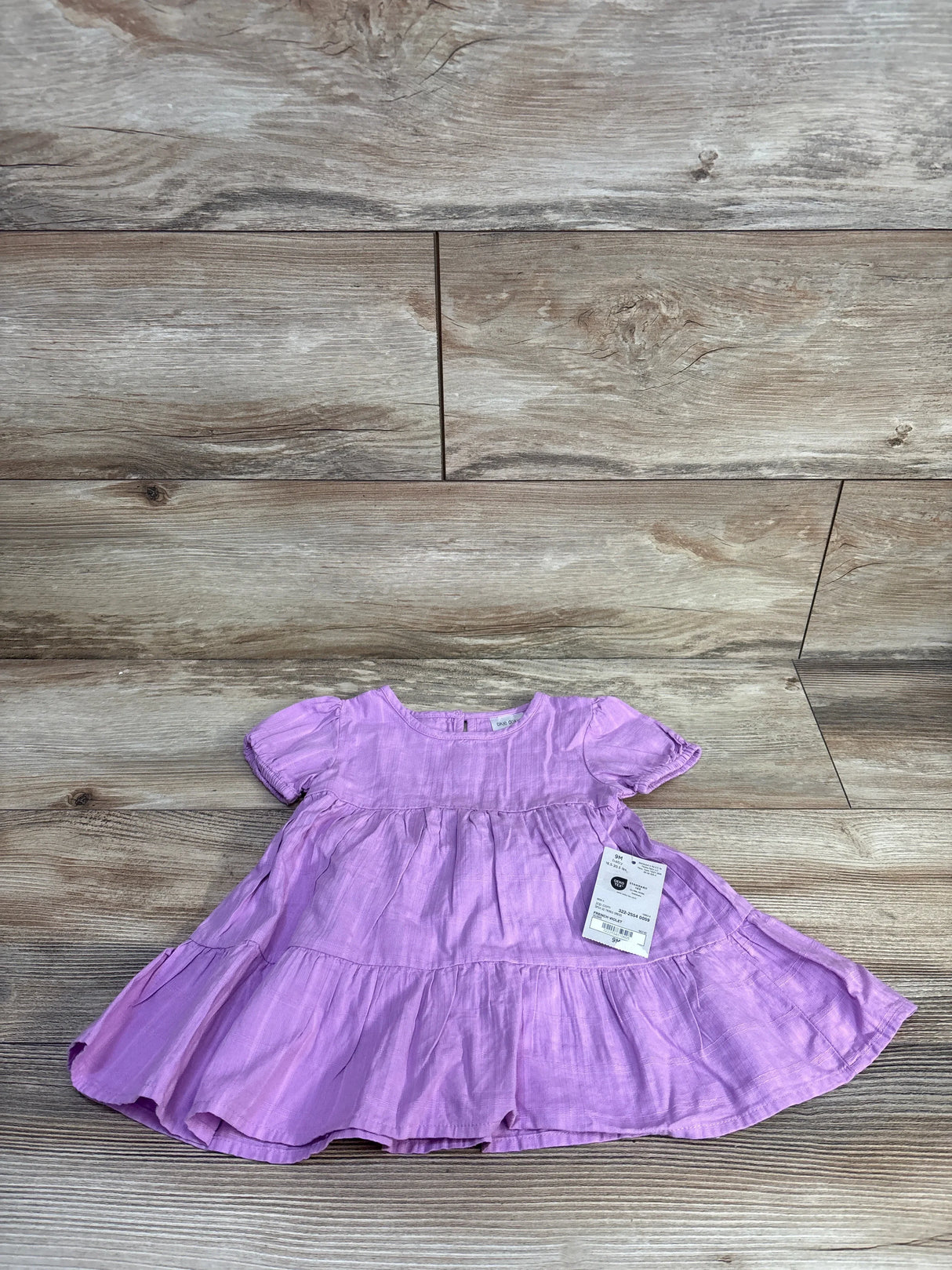 Flat lay of purple Okie Dokie tiered baby dress and matching bloomers showing short puff sleeves and ruffled tiers on a light wood floor
