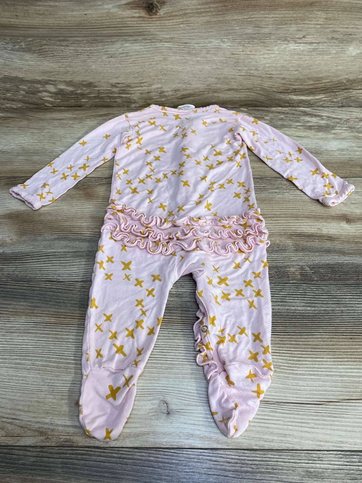 Flat lay of pink Spearmint Love ruffle zip footie with yellow cross print, back ruffles and footed legs on wood background
