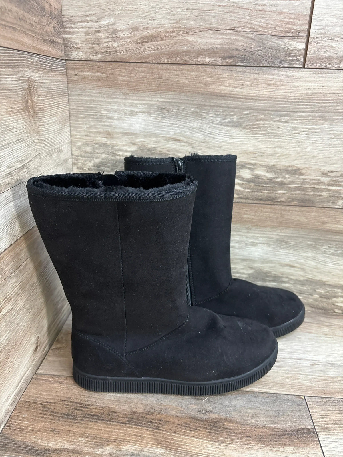 Black faux suede kids boots with side zippers on wood floor background