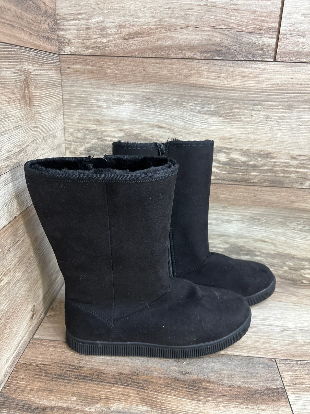Black faux suede kids boots with side zippers on wood floor background