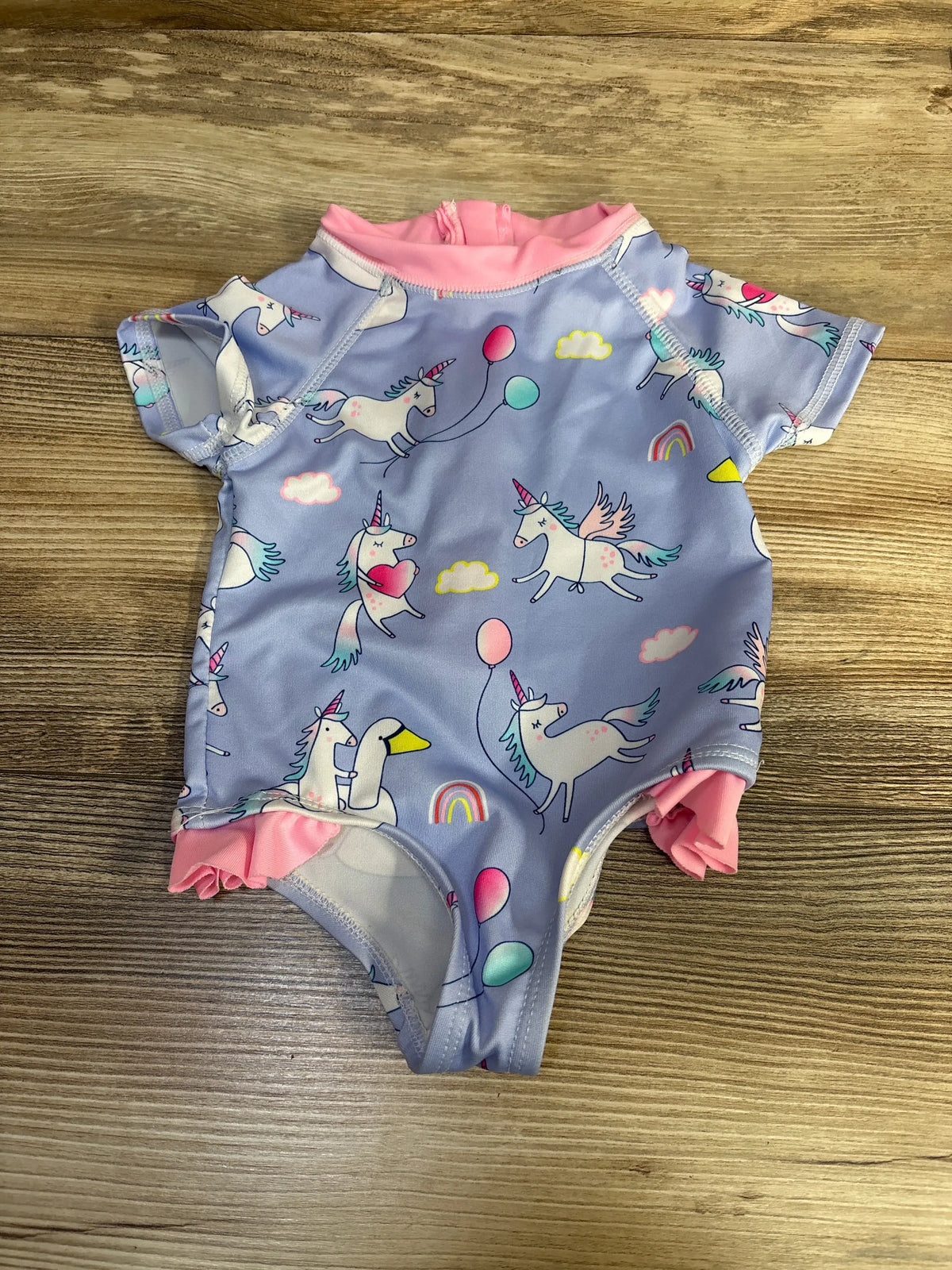 Front view of purple Wippette one-piece unicorn rash guard swimsuit with unicorn print and pink trim on wood